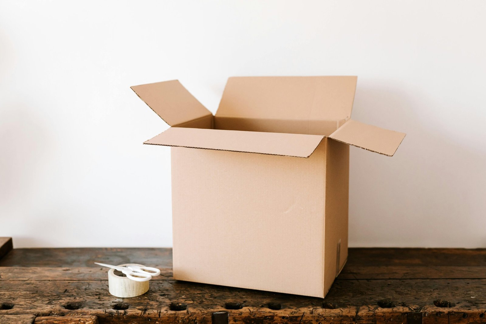 pexels photo 4498152 4498152 Opened cardboard container placed on old wooden desk near tape and scissors before relocation against white wall